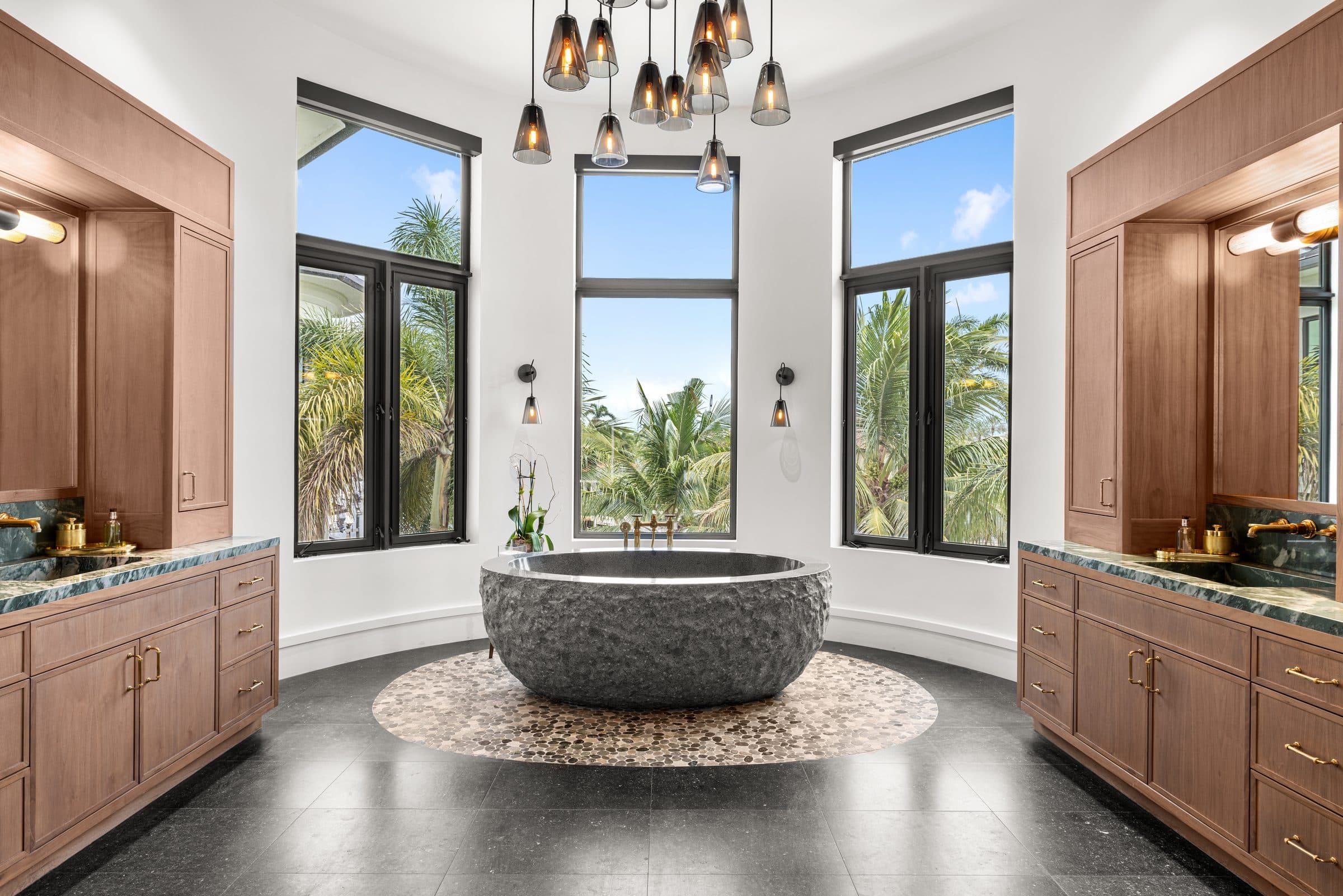 Master bathroom with sculptural stone soaking tub, brass fixtures, and pendant chandelier — the level of detail a house manager oversees