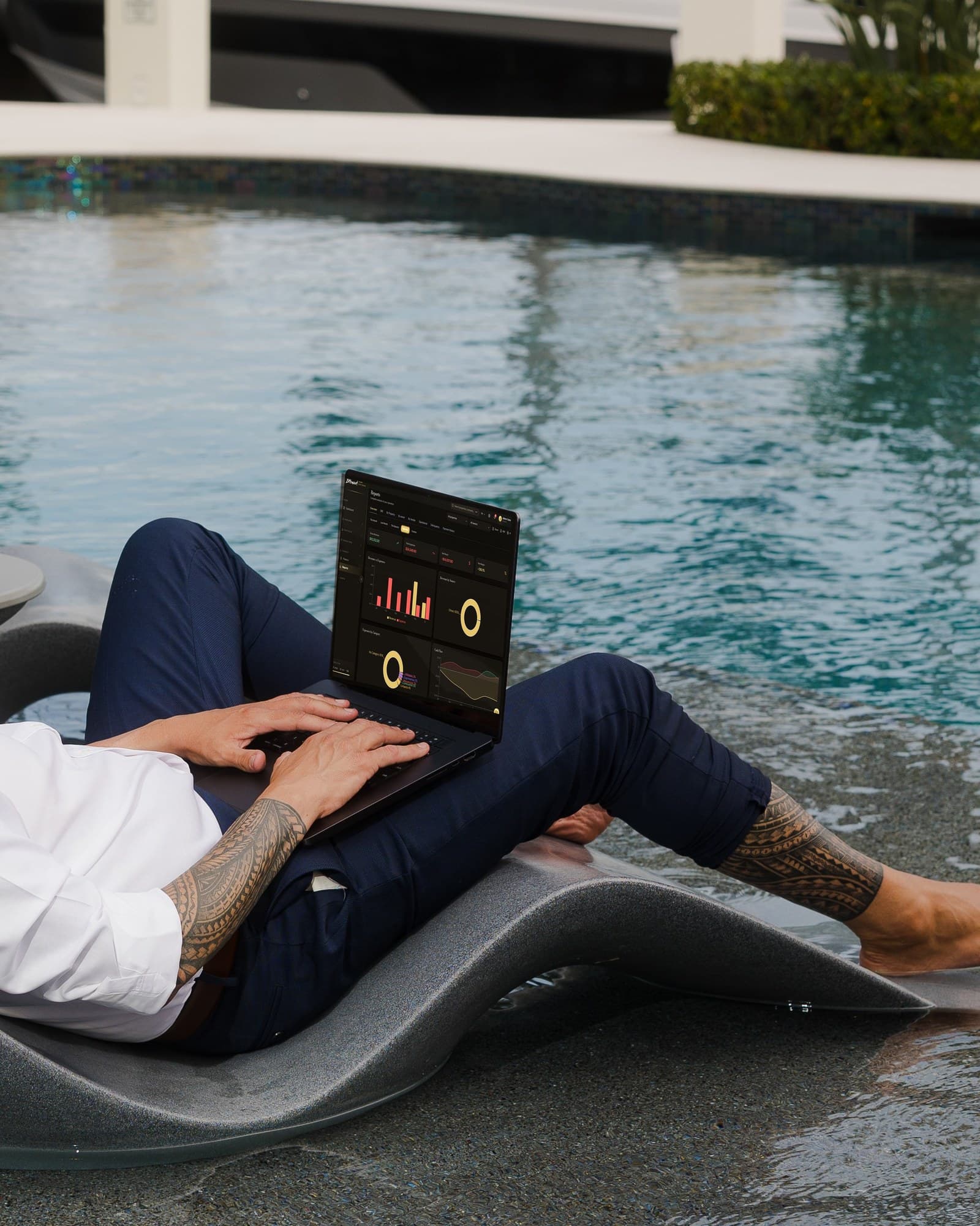 Owner reclining on a poolside lounger, laptop showing the BHS Reports screen with revenue, expenses and cash flow — run your finances from anywhere
