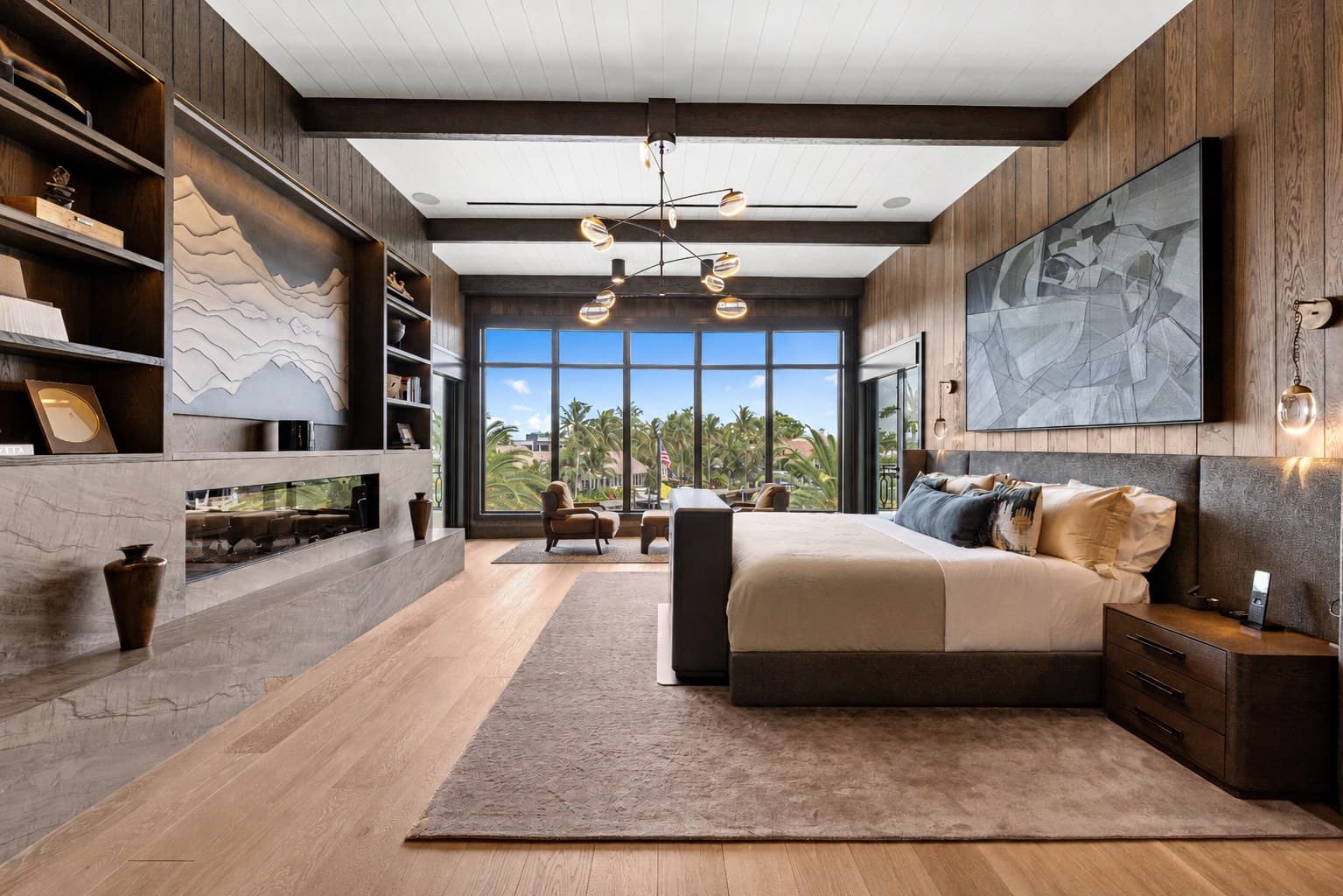 Master bedroom with wood-beam ceiling, sculpted mountain art, gas fireplace, and floor-to-ceiling windows to a palm-lined balcony — the level of detail a homeowner protects