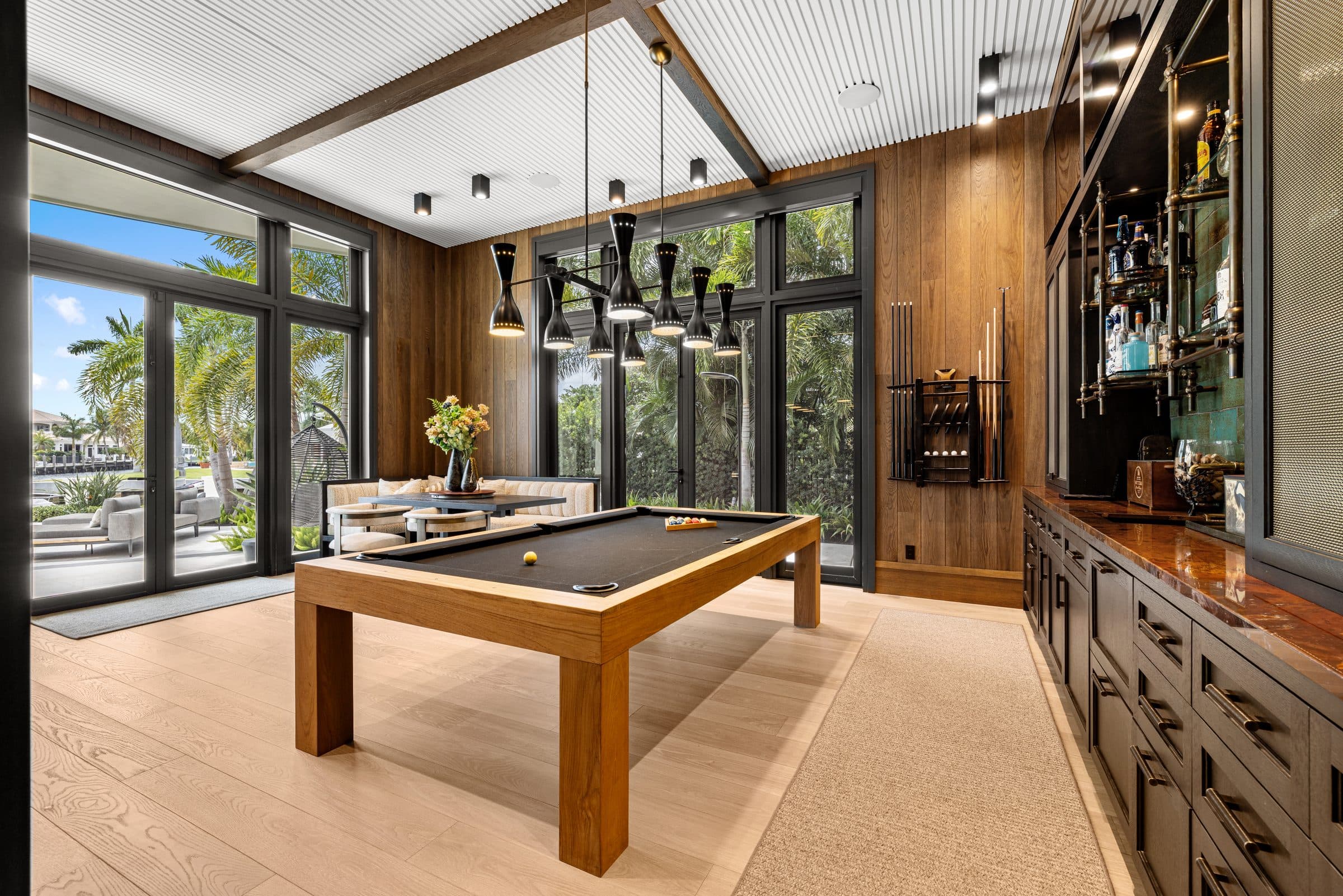 Game room with pool table, custom whiskey bar, and floor-to-ceiling windows opening to the pool — the interior detail buyers want to see